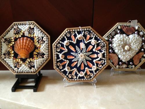 These shell art pieces that resemble sailors valentines are on a board that is painted flat black with a strip of rounded wood for the edges - Slide 19